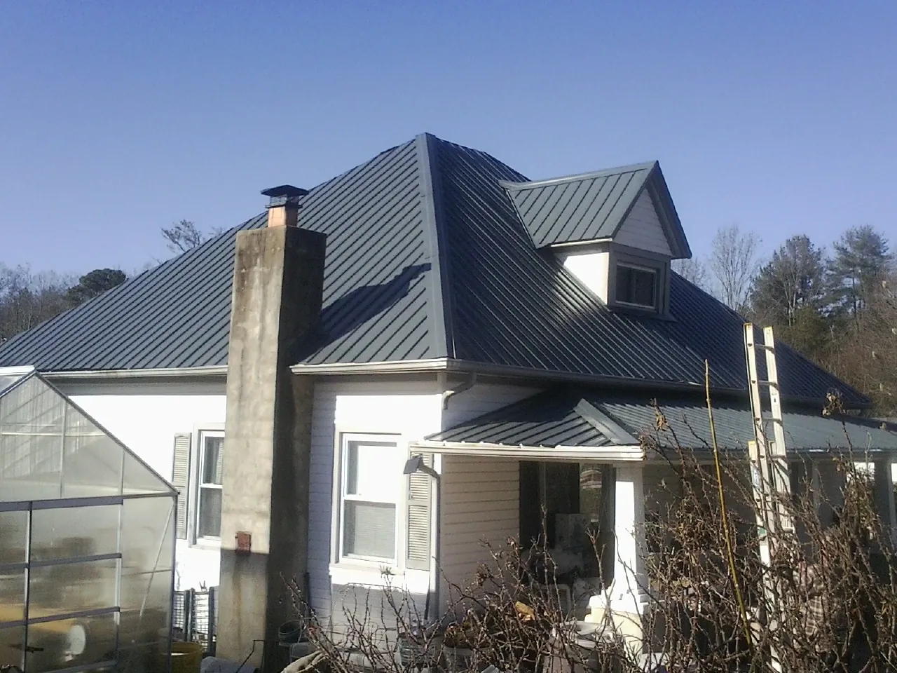 Dark blue standing seam metal roof on a white farmhouse with dormer — Slate & Tile Roof Repair by Roofing Brothers in Lena