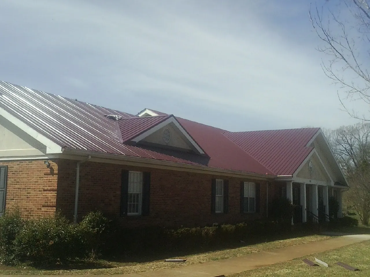 Red metal roof with gabled entries on a long brick building, from a Hail Damage Roof Repair job in Lena