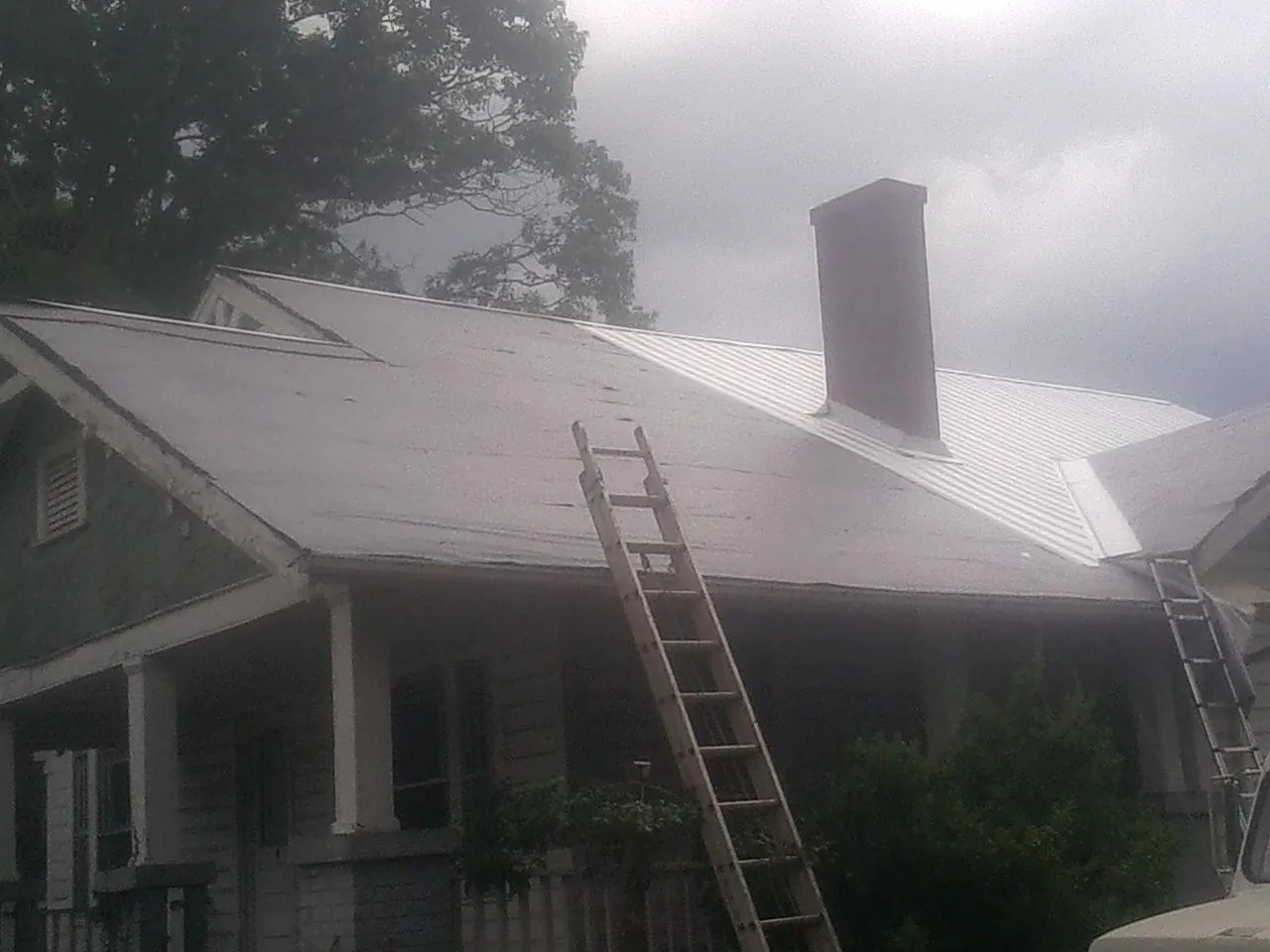 Ladders against a metal roof on an older home with a brick chimney in Lena