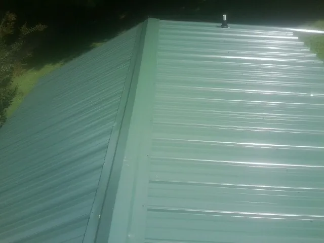 New green metal panels meeting at the ridge of a roof — Flat Roof Repair work by our crew in Lena
