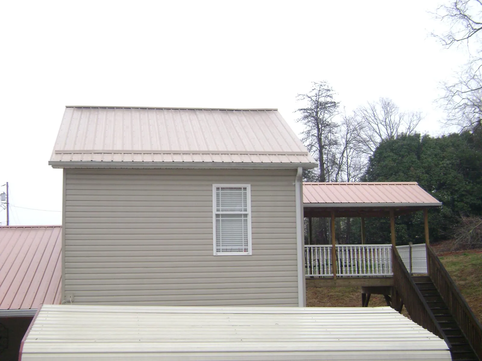 Tan metal roofs on a two story addition and attached porch, from a Roof Replacement job in Lena